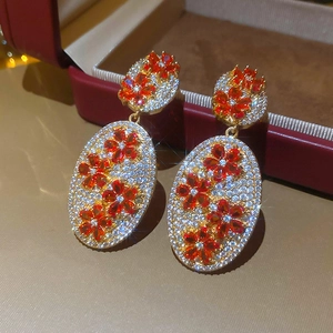 Detail view of gold floral oval earrings with red gems and pavé zircon stones
