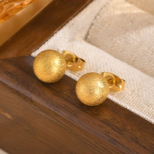 Detail of gold matte ball earrings with sandblasted finish on a wooden display