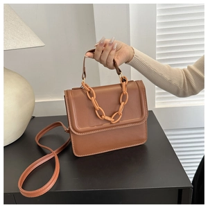 Close-up of brown leather square crossbody bag with stylish matching plastic chain detail