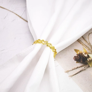Golden hollow heart-shaped napkin ring on white cloth with elegant floral decor