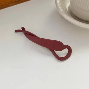 Détail d'une pince à cheveux banane rouge foncé mate sur une surface blanche