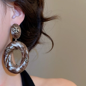 Macro detail of oversized resin hoop earring with metallic gothic cross embellishments