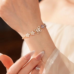 Nahaufnahme eines goldenen Armbands mit Schmetterlings- und Blumendetails und Zirkonia