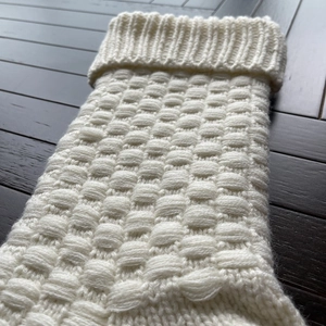 White knitted Christmas stocking with woven texture on a dark wood background