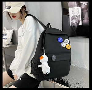 Close-up of black nylon backpack featuring metal badges and a white plush duck pendant