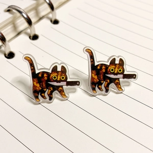 Quirky acrylic tortoiseshell cat earrings with knife design on striped notebook background
