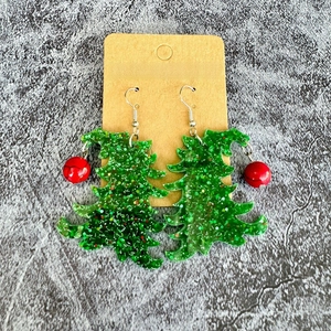Detail of Christmas tree earrings with green glitter acrylic and red bead pendants