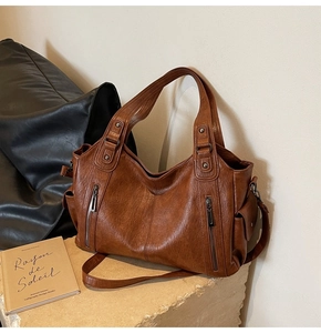 Detailed view of brown leather tote bag with side zipper on a stone pedestal