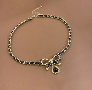 Detail of black faux leather woven chain necklace with bow and spiral pendant