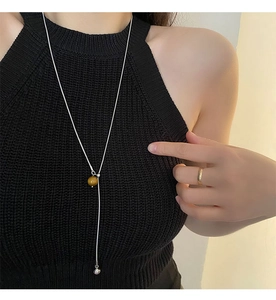Détail d'un long collier en acier titane avec pierre jaune et chaîne argentée sur modèle