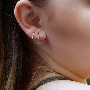 Close-up of minimalist gold hoop earring with a single clear gemstone on female model