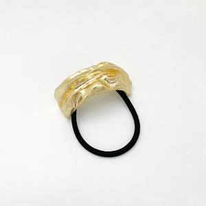 Close-up of golden irregular molten metal texture charm on black elastic hair tie
