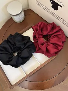 Close-up of black and burgundy satin scrunchies with pleated texture on a tray