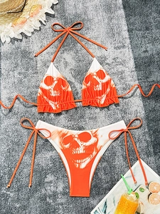 Detailed flat lay of skull print bikini set with orange ruffles and beach accessories
