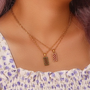 Detail of layered gold twist chains with emerald and pink rectangle maze pendants