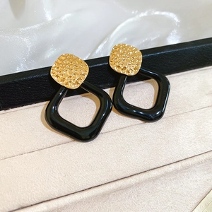 Detail von gehämmertem Goldstecker und glänzend schwarzem Rauten-Ohrring-Anhänger
