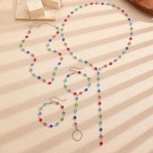 Detail of silver Y-necklace and hand chain set with multi-color rhinestones on beige surface