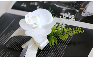Macro detail of white faux orchid boutonniere with elegant cream ribbon for wedding