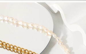 Detail of OT clasp Cuban chain and baroque pearl necklace on reflective mirror surface