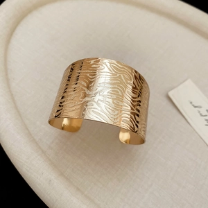 Macro detail of golden irregular wave texture on a wide geometric open cuff bracelet