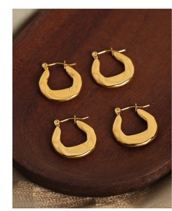 Macro detail of polished gold U-shaped geometric earrings on a rich silk background