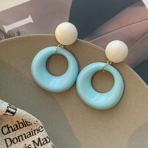 Boucles d'oreilles créoles en résine bleu et blanc avec maillons dorés sur plat beige