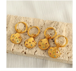 Makroaufnahme goldener Muschelohrringe mit bunten Kristallen auf Steinblock