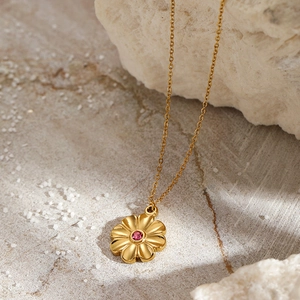 Detail of gold floral pendant necklace with a pink zircon stone on natural rock background