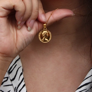 Close-up of golden coin necklace featuring embossed portrait and minimalist ball chain