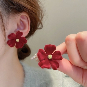 Dettaglio di orecchini a fiore in velluto rosso con centro dorato indossati da modella