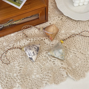 Close-up of three handmade fabric zongzi charms with floral patterns on lace tablecloth