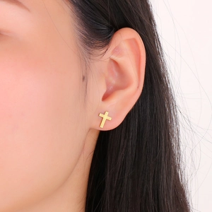 Close-up of a gold cross stud earring worn on model's ear, sleek metal finish