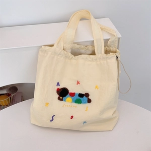 Detail view of cream canvas tote bag featuring colorful animal embroidery and drawstring
