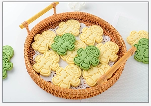 Gingerbread man cookies in beige and green on a round rattan tray with lace paper