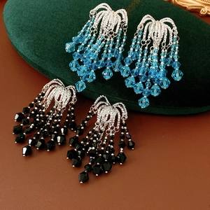 Detail view of light blue and black beaded fringe earrings on a velvet display cushion