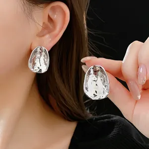 Irregular silver textured earrings with minimalist metal design shown on model and in hand