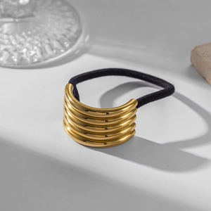 Detail of layered gold metal tubes hair tie with black elastic cord on grey surface