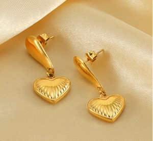Macro shot of gold heart pendant earrings with textured surface on champagne silk fabric