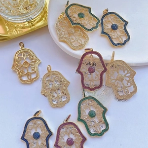Detailed macro shot of hollow Hamsa hand charms with colorful zircon inlays on gold base