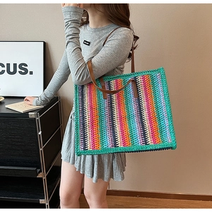 Colorful striped woven tote bag with brown leather straps worn on the shoulder