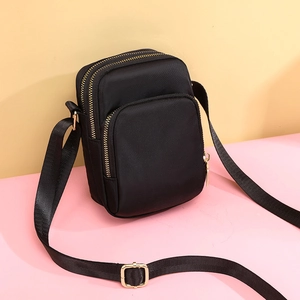 Detail of a black nylon mini crossbody bag showing three gold zipper compartments