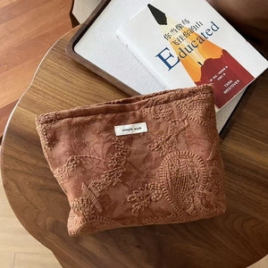 Detailed close-up of brown suede makeup bag with floral embroidery and simple wish label