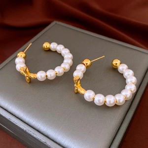 Detailed view of pearl C-shaped earrings with gold bow accents on a gray jewelry box