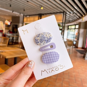 Close-up of three purple floral and checkered fabric hair clips on a display card