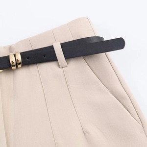 Detail view of beige high-waisted trousers featuring a black belt with gold metal buckle