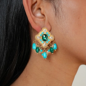 Detail of vintage gold earrings with green crystals and blue beads on a model