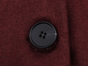 Macro shot of a black four-hole button on dark red knitted fabric detailing the texture
