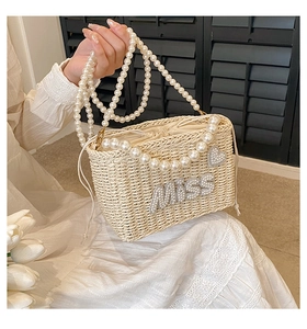 Detail of beige woven straw bag with pearl straps, MISS lettering and rhinestone heart