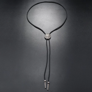 Detail of vintage bolo tie showing silver engraved metal slide and black braided cord