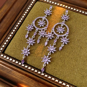 Detail of silver drop earrings featuring purple flower crystals and cascading tassels